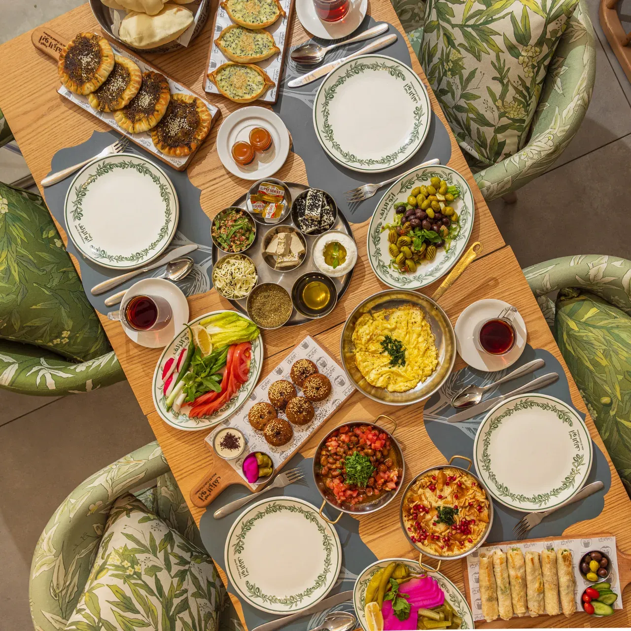 A breakfast table from above, laid with mezze, eggs, falafel and manakish