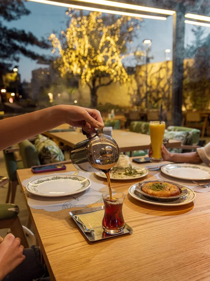 Tea poured at an outdoor table, an olive tree strung with lights behind