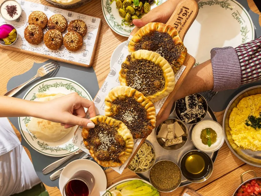 Hands reaching for manakish across a shared breakfast table