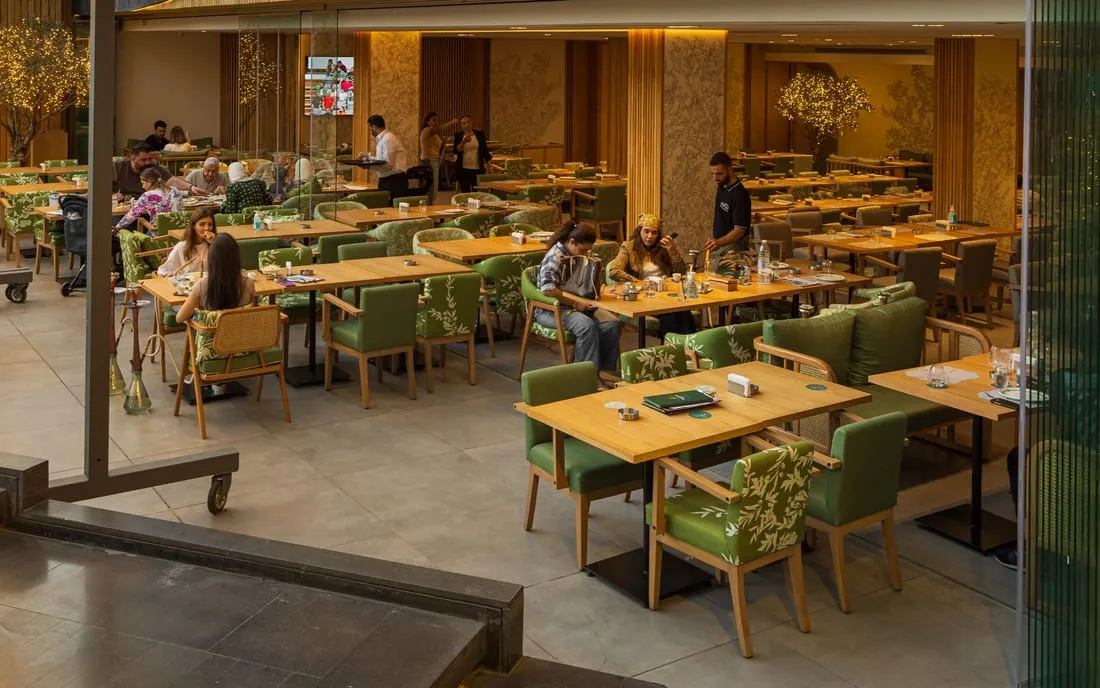 The terrace at dusk, green chairs and wooden tables beneath the lit sign